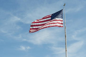 Fototapeta premium waving American flag on a white pylon against blue sky