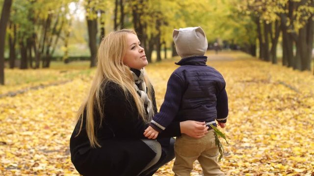 Mother and son walking in the autumn Park on the alley with lots of yellow fallen leaves, the child collects leaves and hugs his beloved mother. 4K.