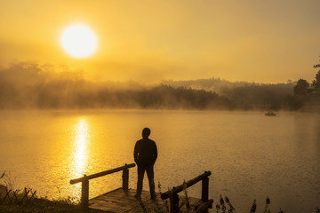 Silhouette Depressed man standing on the houseboat river lake at the sunrise time, dramatic and loneliness concept