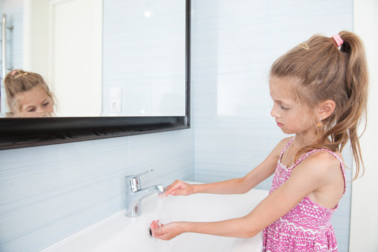 handsome little girl in dress washes her hands in washbasin in bright bathroom
