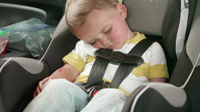 A cute little toddler asleep in his car seat while driving
