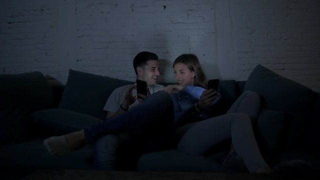 young happy romantic couple using together mobile phone enjoying sitting at home sofa couch browsing and having fun with internet app in communication technology and smart phone addiction concept