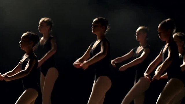 Close-up of a group of flexible girls ballet dancers dancing on stage on a black background, slow motion.
