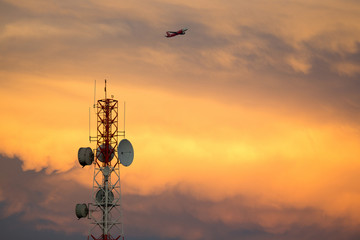 Obraz premium Telecom Signal Tower in sunset and plane is flying through.