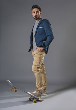 Full length portrait of standing attractive businessman skateboarding with focused look and hands in pockets