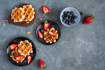 Belgian waffles with fresh strawberry and blueberry on black background. Flat lay, top view, copy space