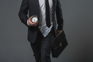 Close up of untidy tardy businessman. Shirt jerked from trousers. He carrying alarm clock and briefcase. Isolated on gray background