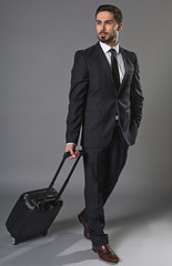 Full length portrait of stylish reflective attractive businessman travelling with suitcase.