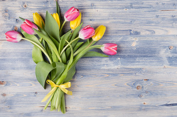 Yellow and red tulips bouquet with ribbon on blue shabby chic wood board. April spring easter background.