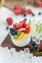 Healthy fruit salad with yoghurt on a wooden plate with ice cubes and fruit as background