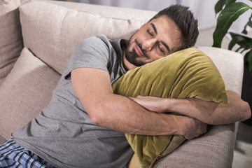 Nice and cozy. Top view of satisfied young man lying and embracing pillow while having nap on sofa