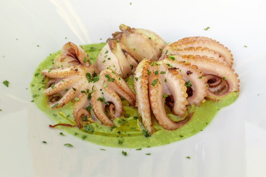 Cena al ristorante: delicatissimo polpo alla brace su crema di piselli nel piatto bianco