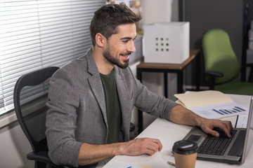 Lovely occupation. Male office worker sitting in front of notebook with smiling face