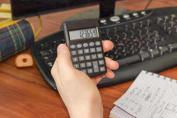Electronic calculator in the hand of schoolboy over the desktop