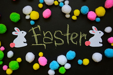 Multicolor frame from woolen Easter bunnies and eggs with written word Easter on the blackboard  background. Top view, flat lay