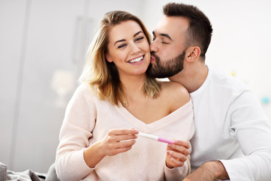 Happy couple with pregnancy test in bedroom