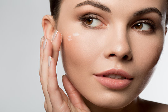 Close up portrait of confident girl applying moisturizer on her face. Isolated
