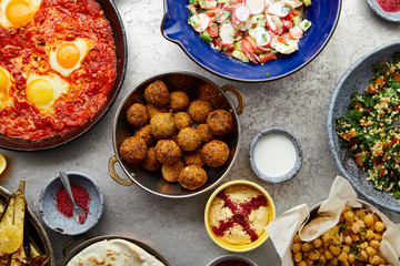 Overhead image of traditional jewish and middle eastern food: falafel, fattoush, tabouli, shakshuka, balila, hummus, roasted eggplants and spicy beetroot dip. Israeli cuisine concept