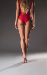 Young sportswoman in red leotard standing with her back and showing slender body