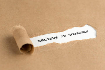 The text BELIEVE IN YOURSELF appearing behind torn brown paper
