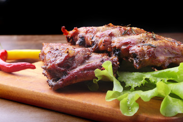 grilled barbecued ribs with lettuce leaves, hot chili pepper and sauce on wooden cutting board.