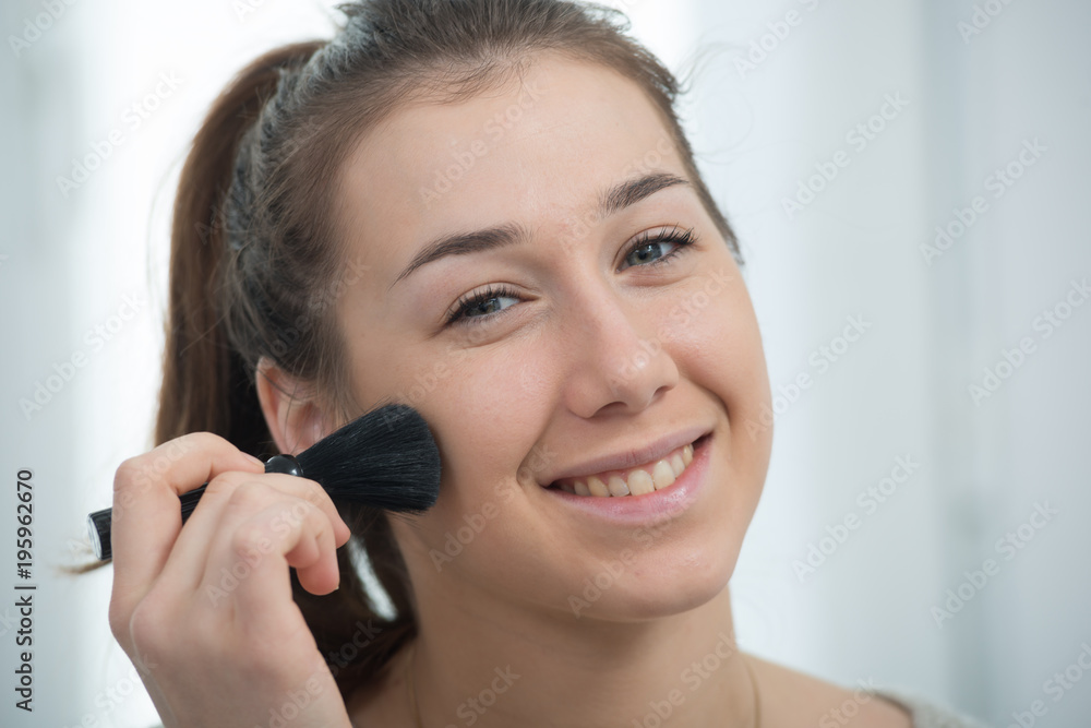 Poster young and smiling woman applying powder on her face