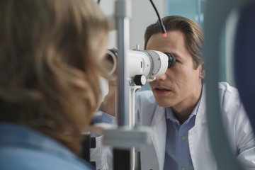 Concentrated doctor examining eyesight of female with special equipment. Diagnostic concept