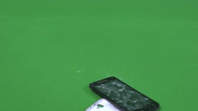 Destruction of the smartphone, phone falls to the surface in slow motion, green background.
