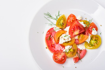 Tomato salad with fresh cheese, olive oil and black pepper on white plate background
