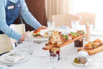 Blurred background. Waiter serving meat dishes on wooden board at restaurant, close up view.