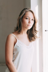 Portrait of pretty young girl on bed in modern Sunny apartment in the morning. Sipping and smiling, drinking coffee and lying on the floor