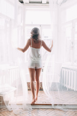 Portrait of pretty young girl on bed in modern Sunny apartment in the morning. Sipping and smiling, drinking coffee and lying on the floor