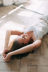 Portrait of pretty young girl on bed in modern Sunny apartment in the morning. Sipping and smiling, drinking coffee and lying on the floor