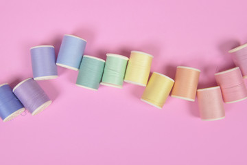 Flat lay of colored thread rolls for sewing on pink background, Sewing and needlework concept.
