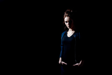 A fashion girl holds her hands in jeans pockets on a black background in a low key with space for text