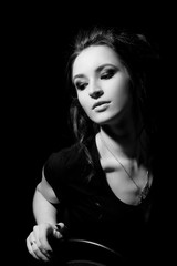 Girl in black T-shirt and with make-up sits on chair and looks down on black background close-up