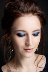 Student portrait of a brunette girl with makeup on closed eyes and a stylish hairstyle on a black background close-up