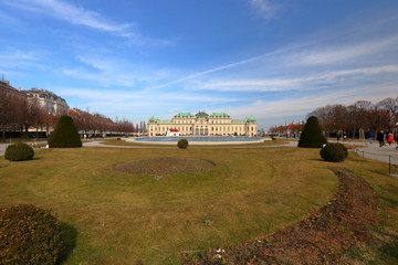 Panoramiczny widok ogrodu pałacu Belvedere w Wiedniu, Austria, budynek pałacu w tle, błękitne niebo z malowniczymi chmurami, wczesna wiosna