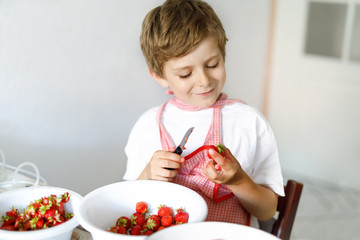 Little blond kid boy helping and making strawberry jam in summer