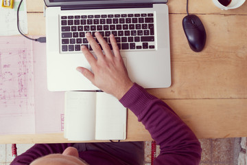 Man using laptop and notes, papers on a rustic table.