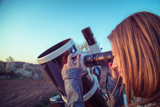 Cute young woman holding astronomical telescope and looking at the sky.