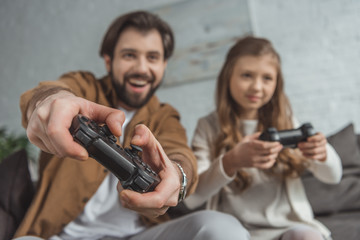 smiling father and daughter playing video game with focus on joysticks