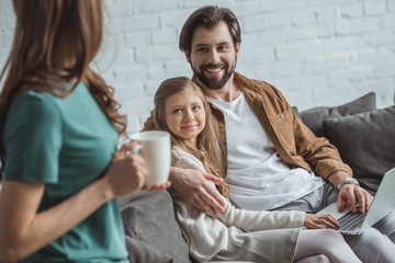 father hugging daughter and looking at mother with cup of coffee