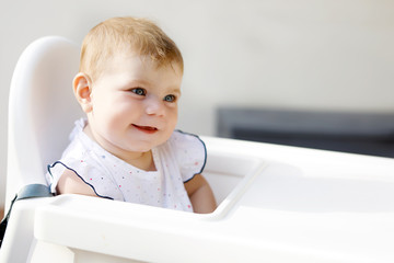 Portrait of cute little baby girl sitting in high chair and waiting for feeding