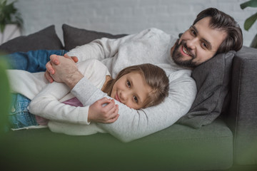 Fototapeta na wymiar father and daughter lying on sofa and looking at camera