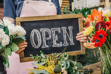 Woman holding open sign among flowers bouquet on florist shop