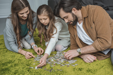 parents and daughter connecting puzzle pieces on carpet in living room