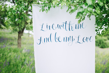 white linen with the inscription about love hanging on a tree against the background of a flowering meadow
