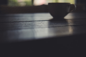 Silhouette image of coffee cup on vintage wooden table in cafe with blur background