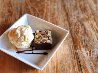 rownie with ice cream in white  Square plate on the wooden table. Natural light and copy space . Delicious and unhealthy menu.